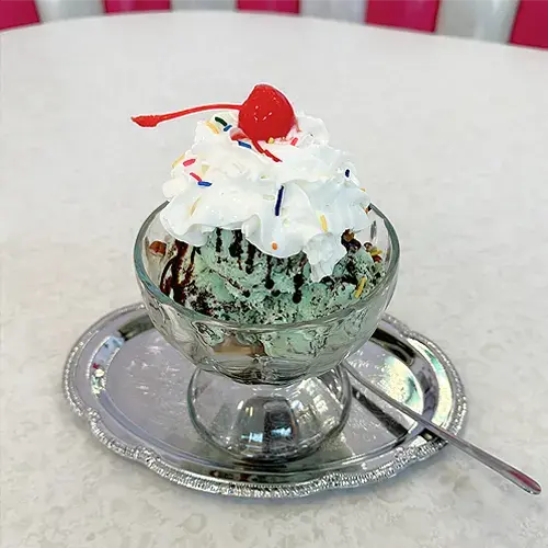 Hands holding a sundae in a glass bowl with whipped cream and a cherry